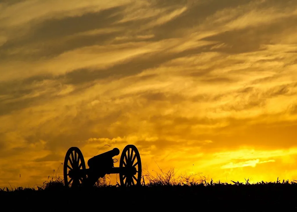 Silhouette of an old field cannon on a ridge against a burning orange sunset sky