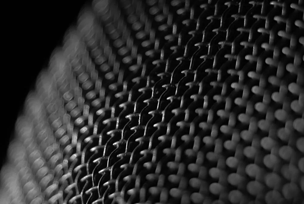 Close-up black and white photo of tightly woven wire mesh curving away into shadow