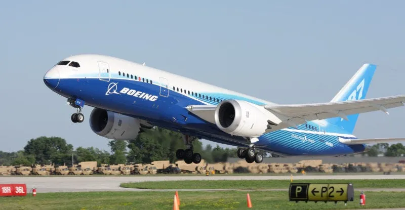 Blue and white Boeing Dreamliner lifting off a runway, a nod to shipping builds out the door