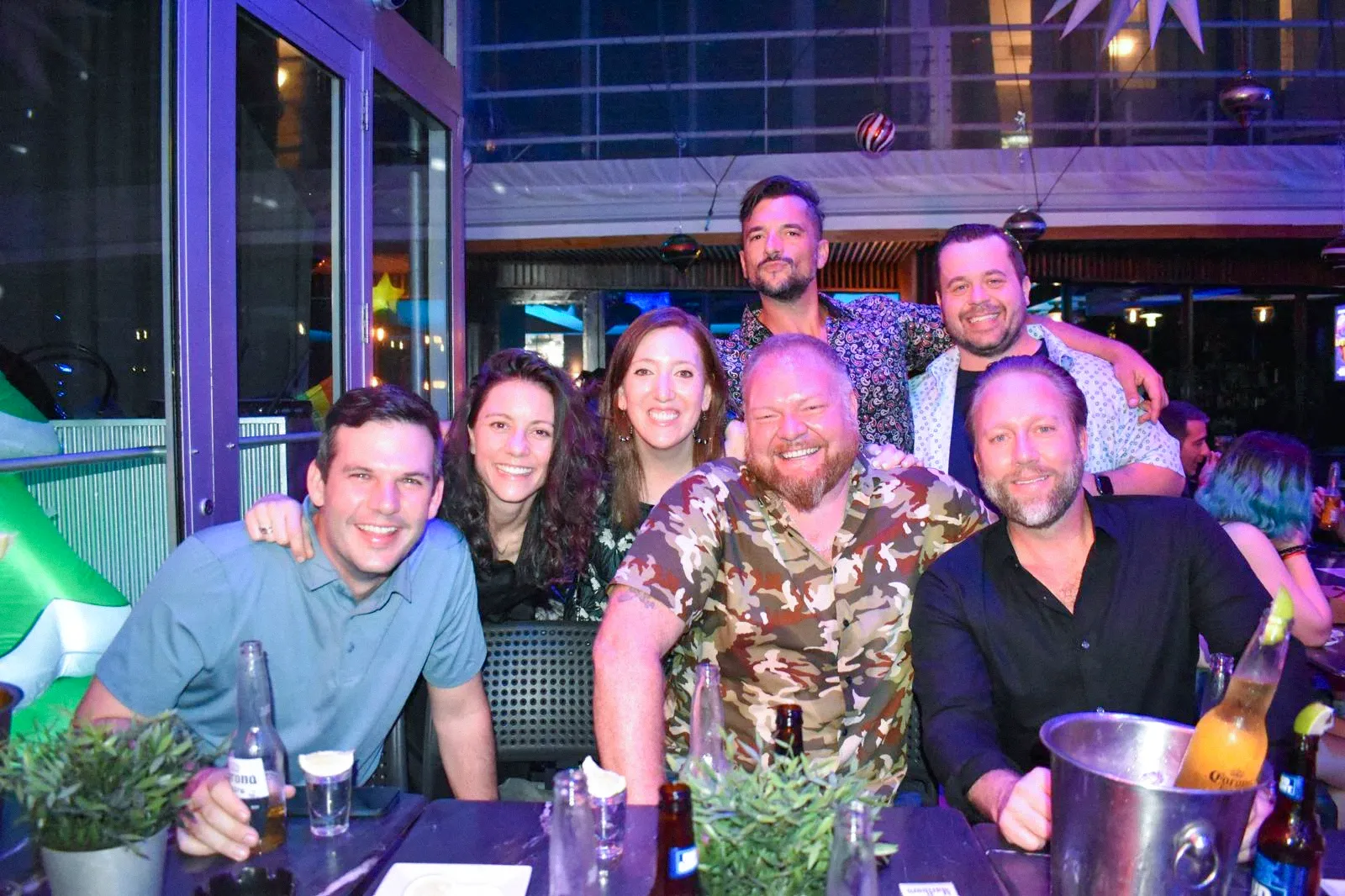 Seven Tarmac colleagues crowded together and smiling around a table at an evening bar gathering