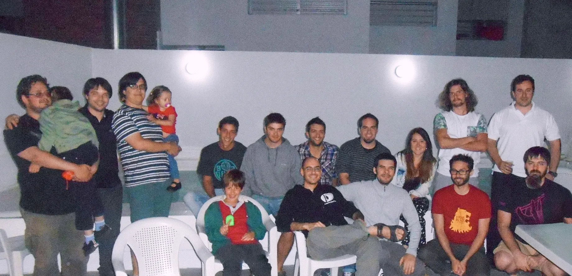 Early Tarmac team photo at a night-time get-together, colleagues seated with partners and kids
